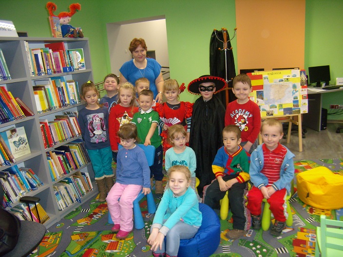 Przy regale z książkami stoi bibliotekarka i grupa dzieci w przebraniu Zorro i Hiszpańskiej tancerki. 