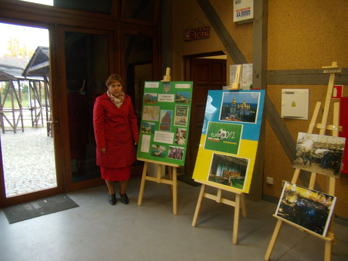 Bibliotekarka z MBP w Działdowie stoi przy wystawie fotografii kultury i tradycji Ukrainy.