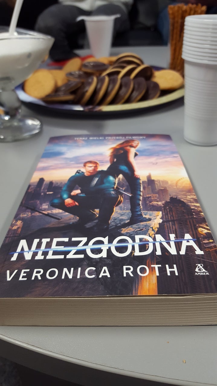 Na stoliku ciasteczka, kubeczki do picia i książka pt. ,,Niezgodna'' Veronici Roth.