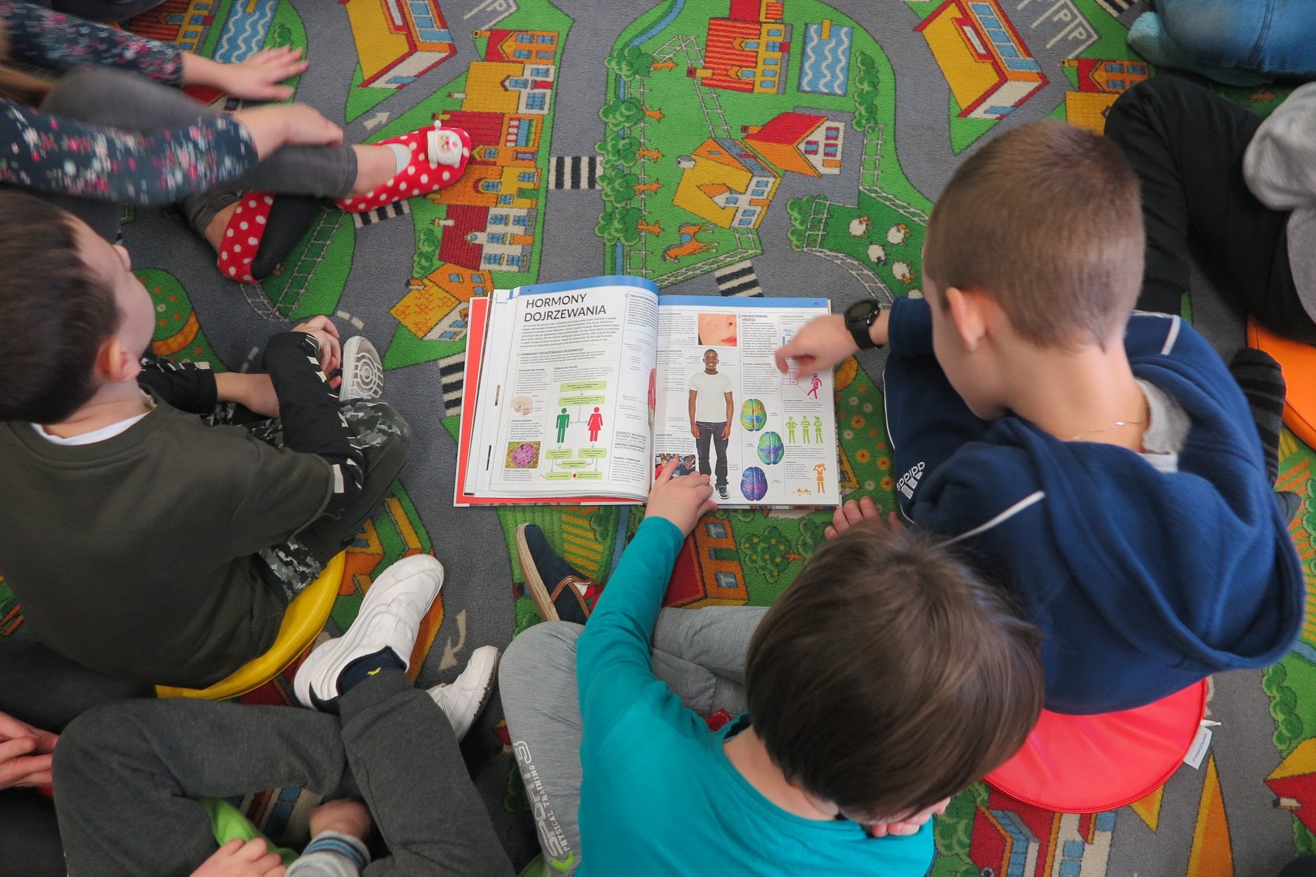 Wnętrze biblioteki (Klub Malucha) czworo dzieci przegląda książkę.