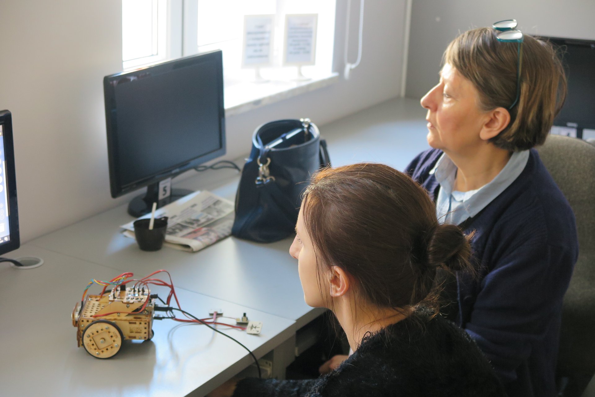 Wnętrze biblioteki (mediateka) zajęcia z robotami prowadzi pan Paweł przy komputerach dwóch uczestników oraz ich robot LOfi