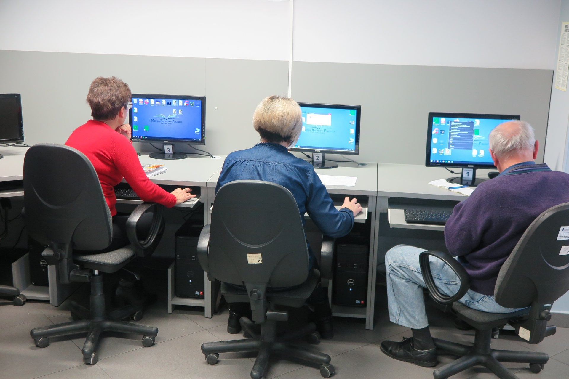 Wnętrze biblioteki (miediateka) trzech uczestników siedzi przed komputerami na kursie komputerowym. 