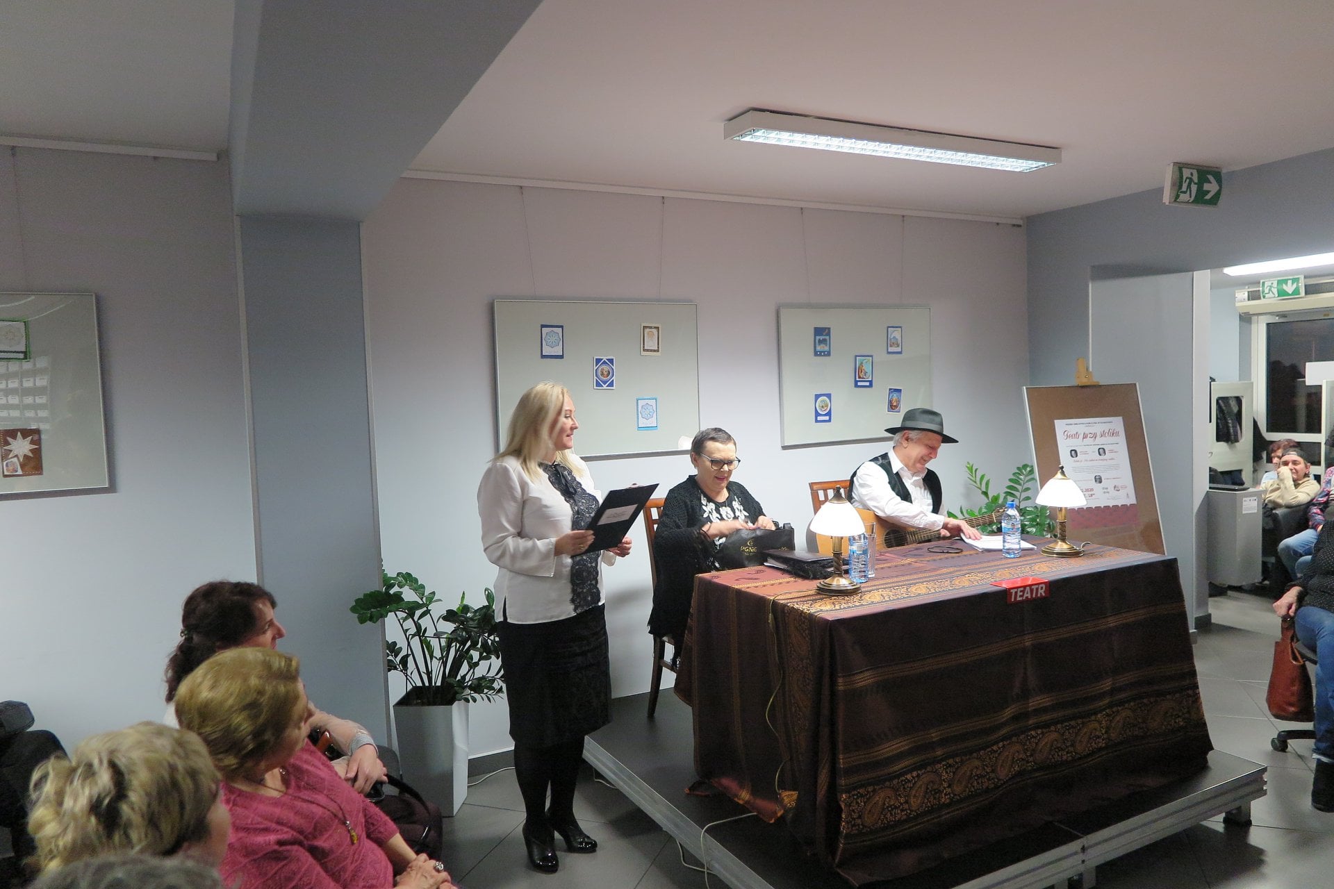 Wnętrze biblioteki. Pani dyrektor Justyna Lytvyn oraz przy stoliku TEATR Wiesława Szymańska i Marian Czarkowski.