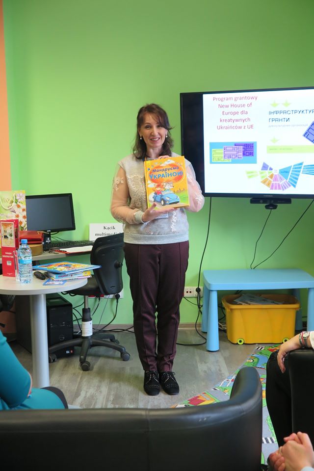 Wnętrze biblioteki przy monitorze pani Valentina Bernatska z Ukrainy trzyma książkę dla dzieci. 