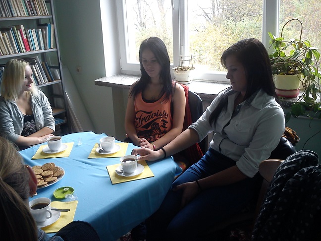 Przy stoliku siedzą członkowie DKK ZS Malinowo wspólnie omawiają książkę "Dziecko Ulicy", na stole kawa i ciastka.