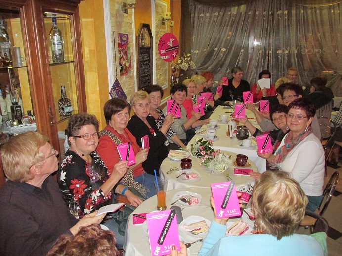 Przy stolikach siedzą członkowie DKK UTW wspólnie świętują 5 lat istnienia oraz omawiają kolejną książkę Małgorzaty Gutowskiej – Adamczyk: "Cukiernia pod Amorem".