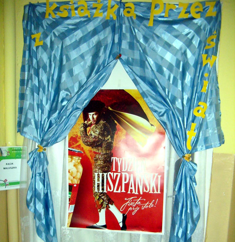 Na drzwiach wisi czerwony plakat z napisem Tydzień Hiszpański oraz niebieska dekoracja z żółtymi literkami Książką przez Świat.