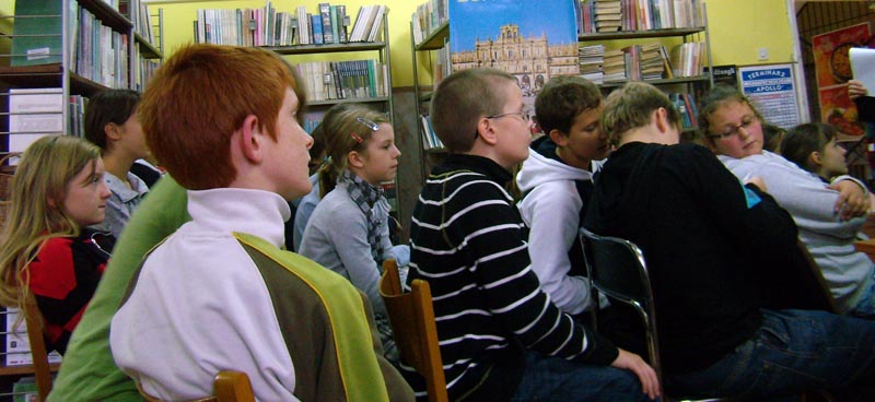 Wnętrze biblioteki,grupa dzieci siedzi na krzesełkach.