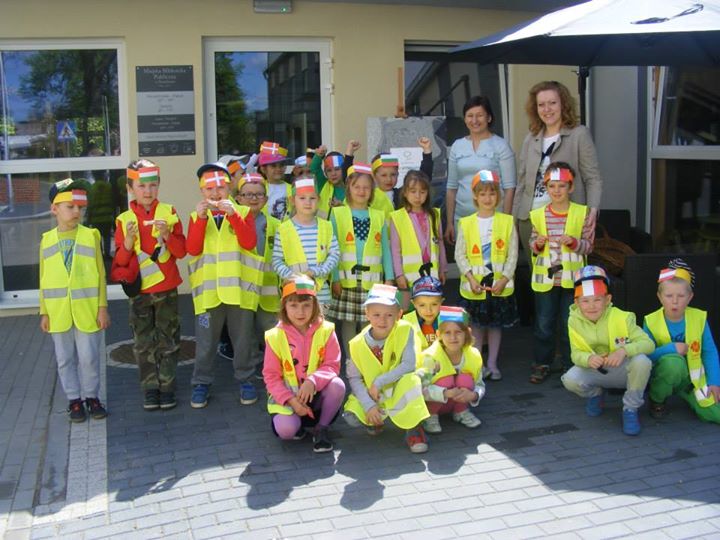 Na placu przed MBP grupa dzieci w żółtych kamizelkach podczas Otwartych Funduszy Europejskich w bibliotece.