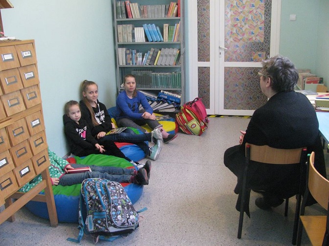 Wnętrze biblioteki, pani Ewa Sotomska i grupa dzieci z DKK wspólnie omawiają  książkę Beaty Ostrowickiej " Jest taka historia".