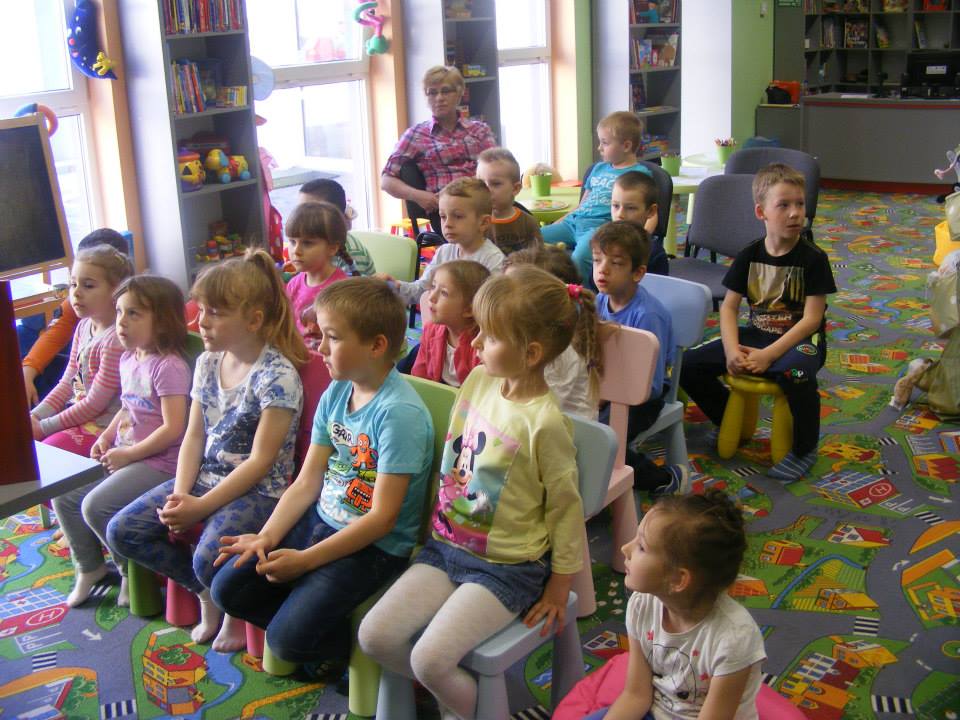 Na krzesełkach siedzą dzieci biorą udział w zajęciach  „W świecie bajek i legend”. 