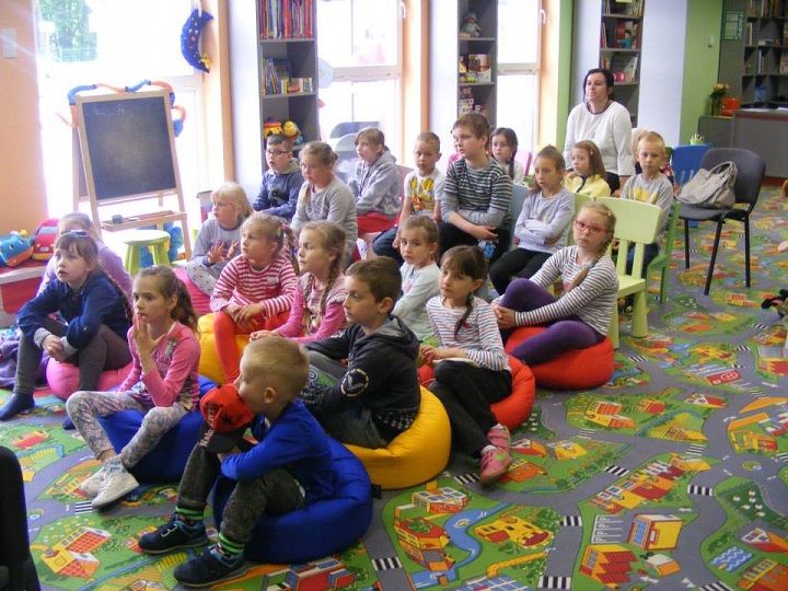 Grupa dzieci siedzi na kolorowych pufach, bibliotekarka Ania prowadzi lekcję na temat Unii Europejskiej. 