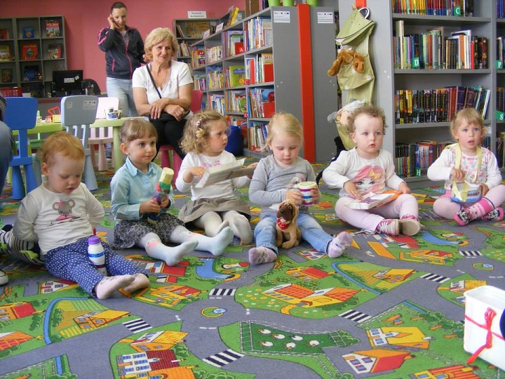 Na kolorowej wykładzinie siedzi sześcioro dzieci , wszystkie trzymają instrumenty przygotowane z pomocą opiekunek.