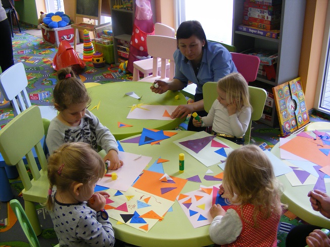 Grupa dzieci wycina i przykleja kolorowe trójkąty. 