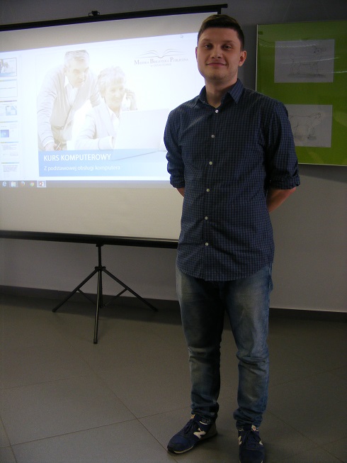 Prowadzący kurs komputerowy, w tle wyświetlona prezentacja dotycząca tego wydarzenia.