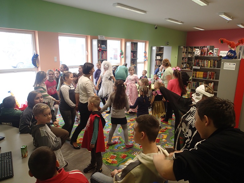Grupa dzieci tańczy z bibliotekarką Anią do utworów muzycznych.