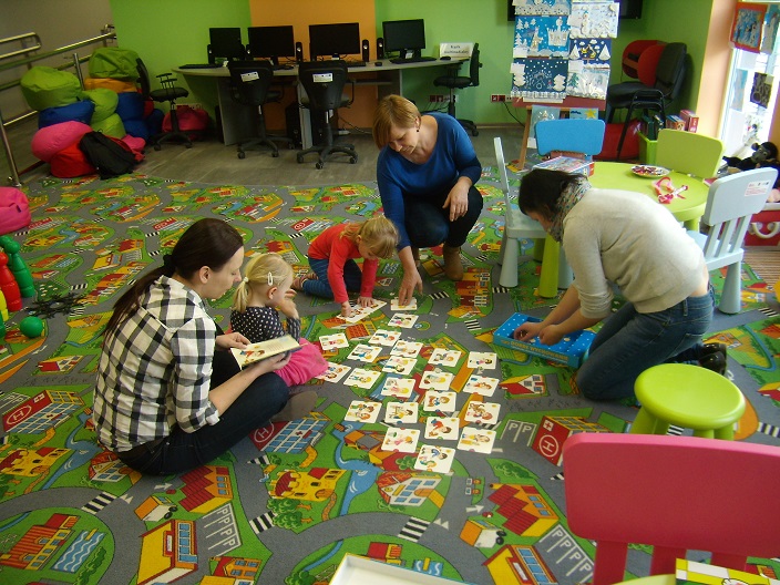 Dwie dziewczynki z opiekunkami i bibliotekarką Anią wspólnie układają na dywanie bajkowe karty.