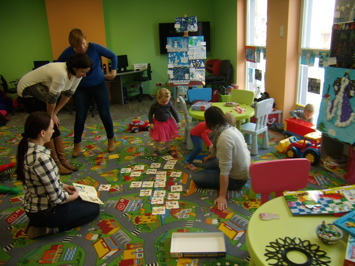 Dwie dziewczynki z opiekunkami i bibliotekarką Anią wspólnie układają na dywanie bajkowe karty.