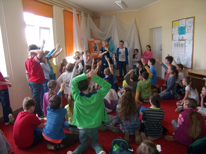 Wnętrze biblioteki, grupa dzieci na zajęciach z pisarką Wiolettą Piasecką.