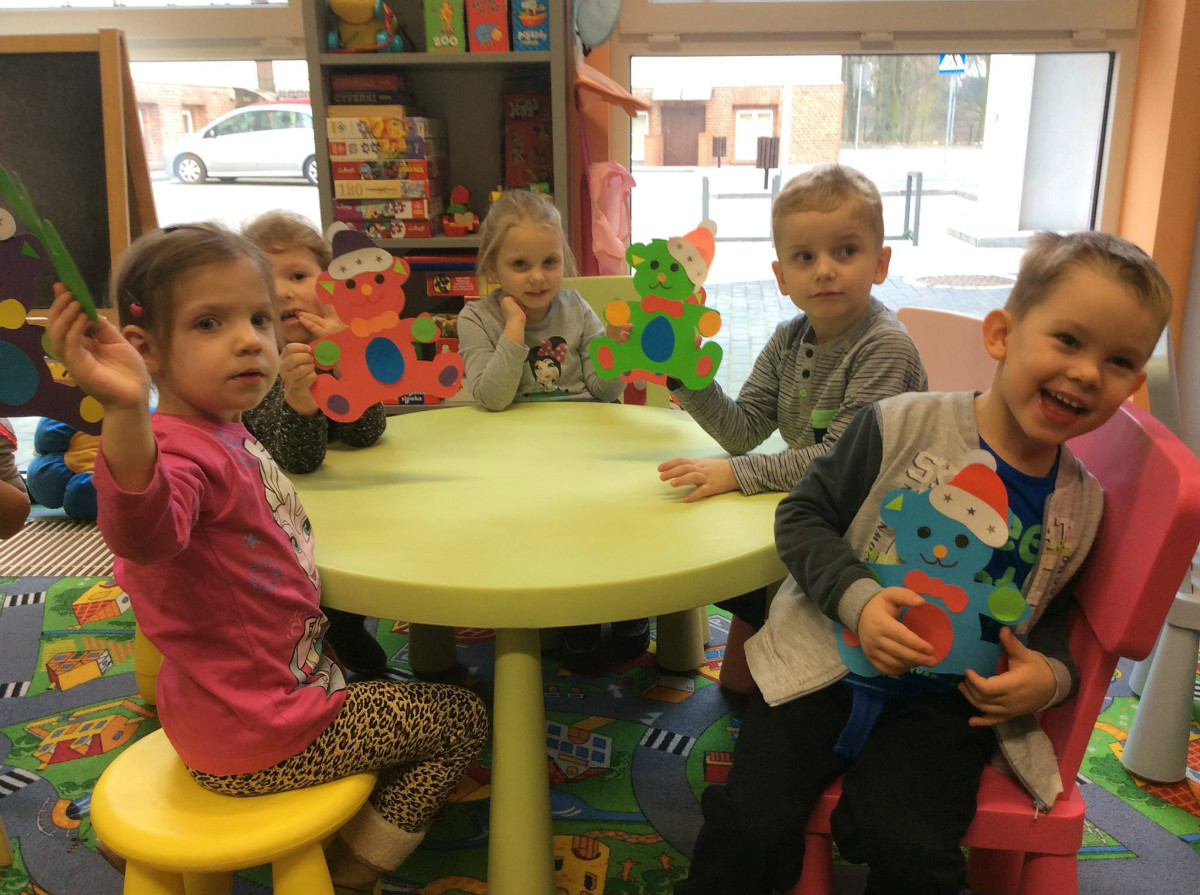 Przy stoliku siedzą dzieci prezentują ozdobione misie.