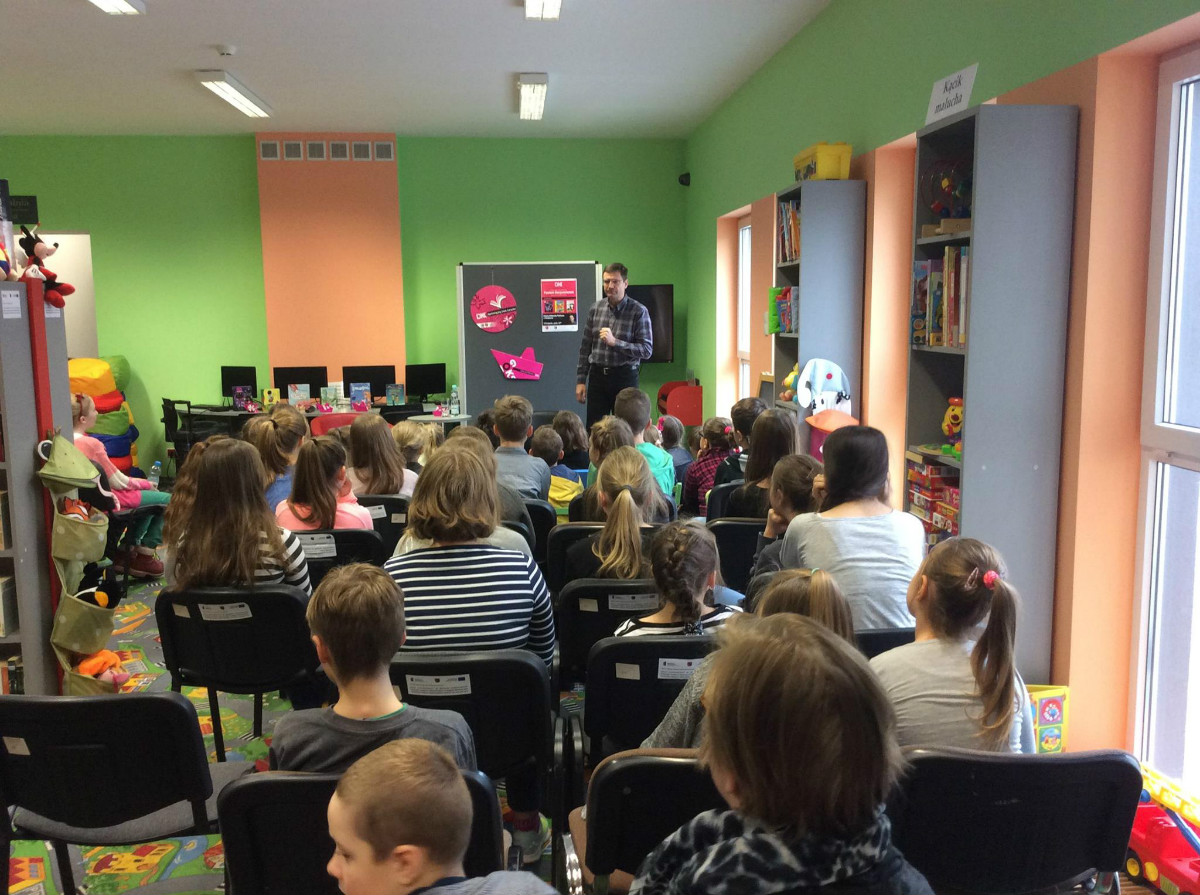 Wnętrze biblioteki, na krzesełkach siedzą dzieci biorą udział w spotkaniu w ramach DKK z Pawłem Beręsewiczem.