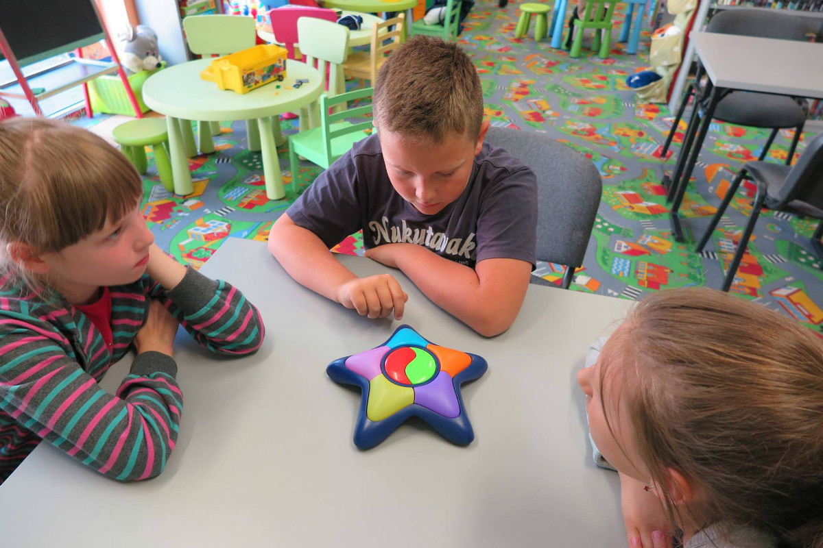 Przy stoliku siedzi trójka dzieci razem bawią się kolorową gwiazdą.