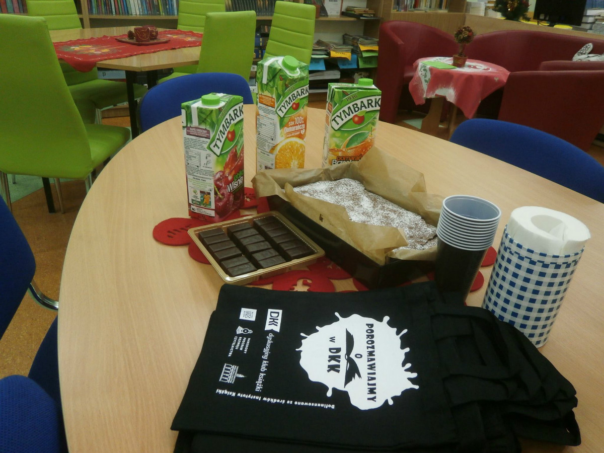 Na stoliku poczęstunek dla DKK SP2 soki,ciasto,czekoladki i czarne torebki z napisem ''Porozmawiajmy o książkach w DKK''. 