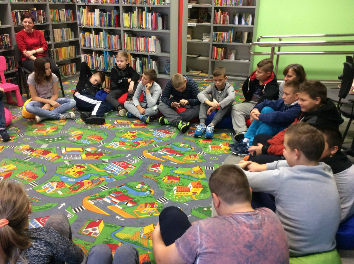 Wnętrze biblioteki. W kole siedzi młodzież ze SP z Klęczkowa razem słuchają opowiadań z książek "Rady nie od parady" Małgorzaty Strzałkowskiej oraz "12 ważnych opowieści.