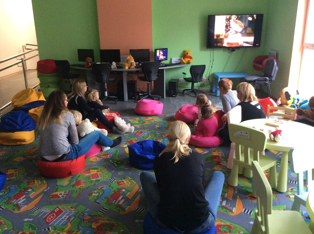 Grupa dzieci z opiekunkami wspólnie ogląda bajkę o misiu.