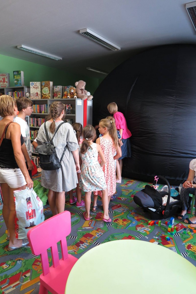 Wnętrze biblioteki. Po kolei dzieci wchodzą do mobilnego planetarium na projekcję filmu o kosmosie.