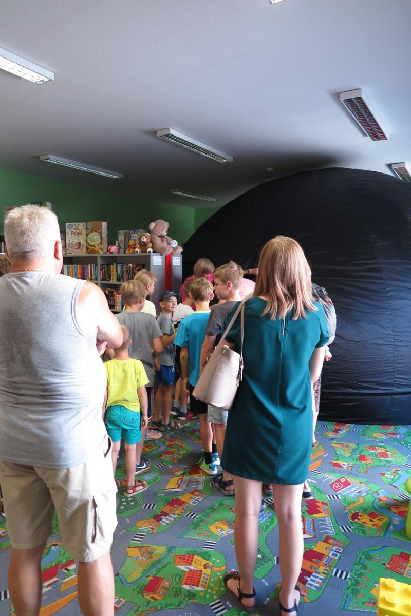 Wnętrze biblioteki. Po kolei dzieci wchodzą do mobilnego planetarium na projekcję filmu o kosmosie.