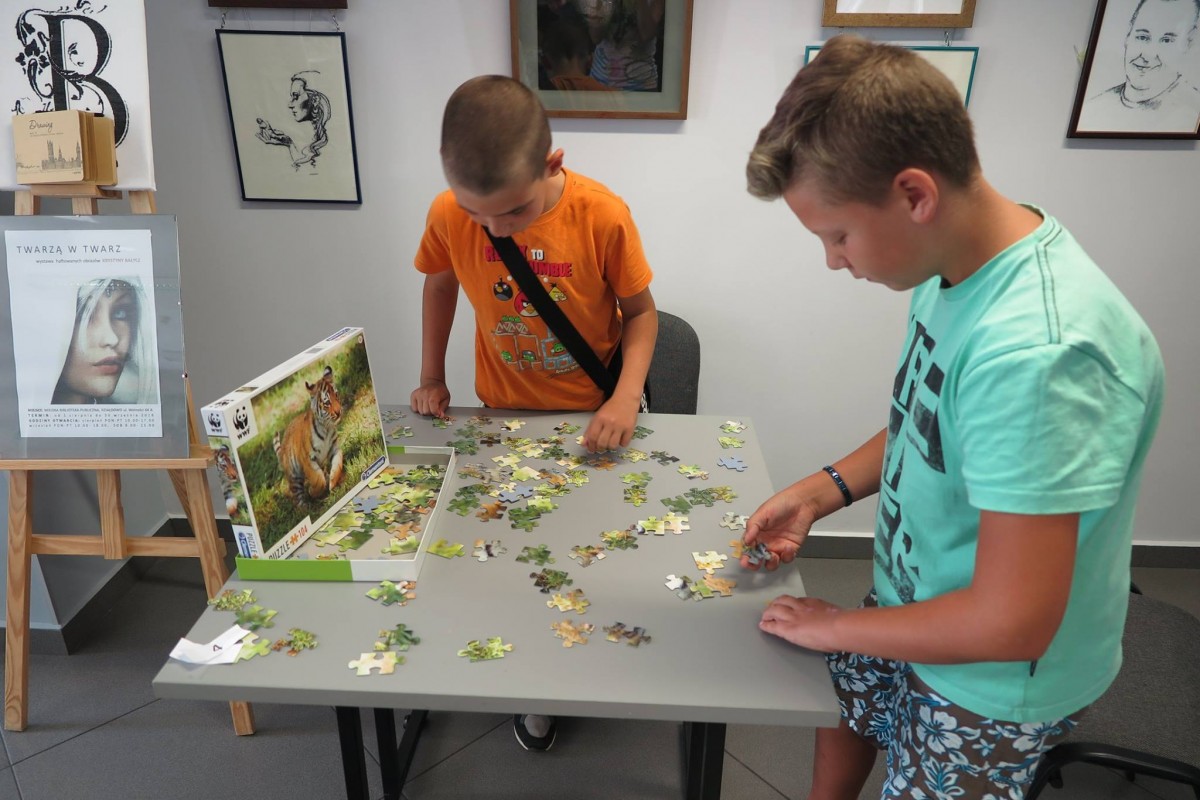 Wnętrze biblioteki,mediateka. Przy stoliku dwaj chłopcy układają puzzle.