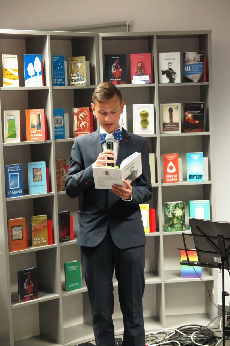 Przy regale z książkami uczeń szkoły z Malinowa czyta wiersze poety Krzysztofa Tabaczki. 