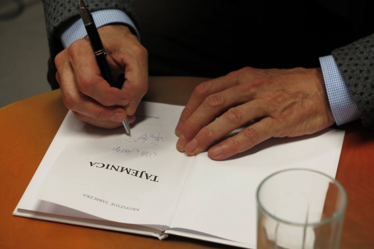 Poeta Krzysztof Tabaczka podpisuje dla gościa książkę ''Tajemnica'' swojego autorstwa. 