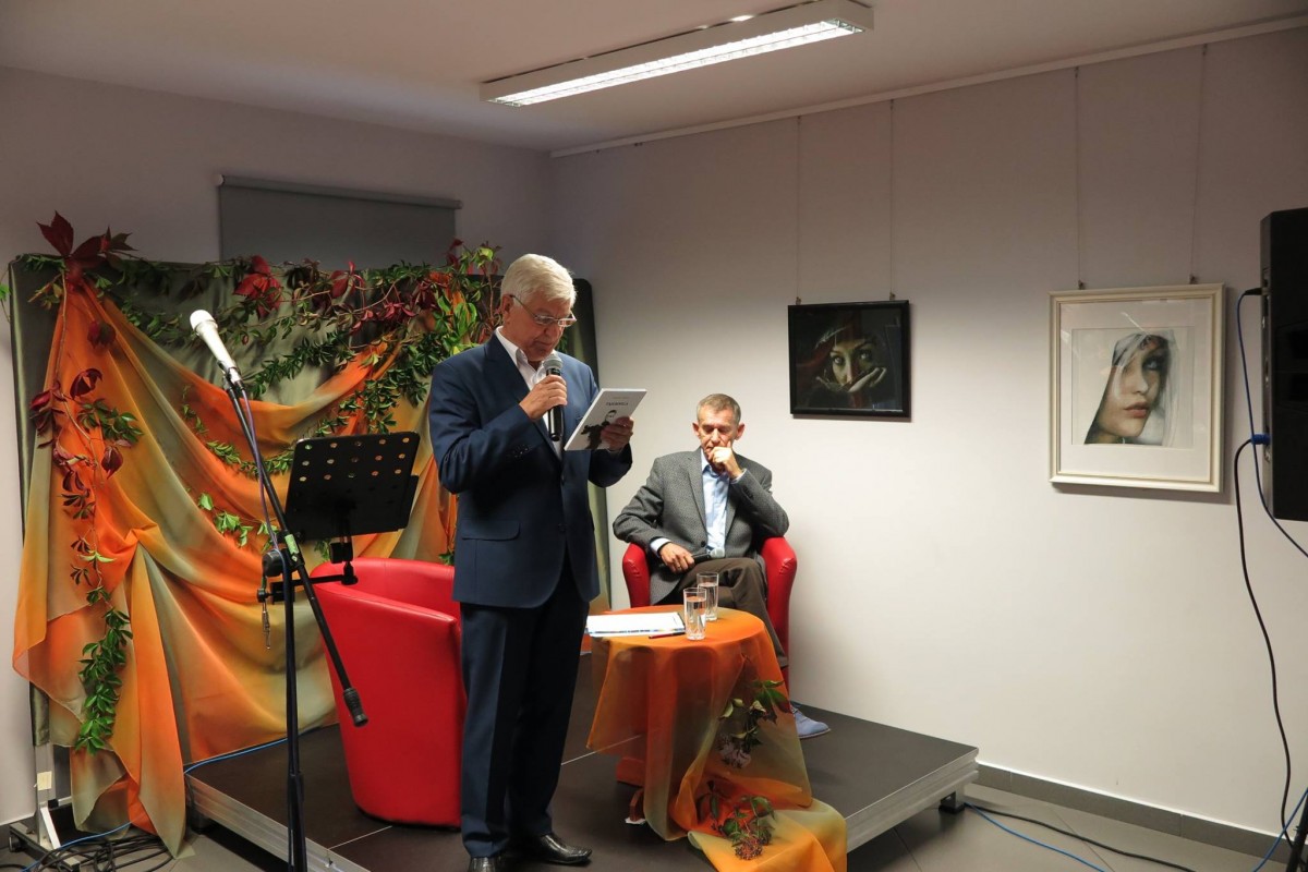 Na scenie w MBP z mikrofonem pan Elek Cichosz , na czerwonym fotelu siedzi poeta Krzysztof Tabaczka. 