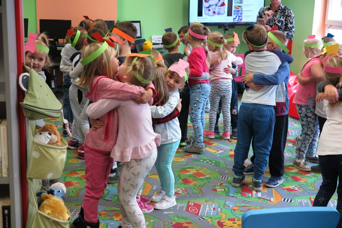 Wnętrze biblioteki. Na kolorowej wykładzinie dzieci tańczą do piosenek o misiach. 