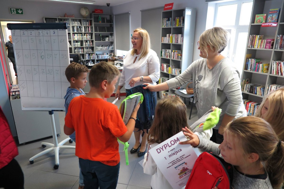Wnętrze biblioteki,mediateka. Bibliotekarka Dorota Kusik i dyrektor Justyna Lytvyn wręczają nagrody dzieciom za udział w bajkowej grze miejskiej. 