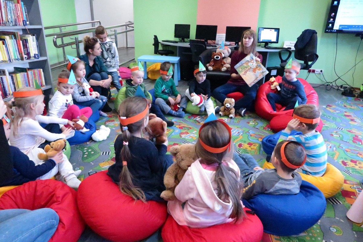 Wnętrze biblioteki. Na pufach siedzą dzieci i słuchają opowiadania o misiu Bysiu, który nie chciał się dzielić, czyta bibliotekarka Ola Cybulska.