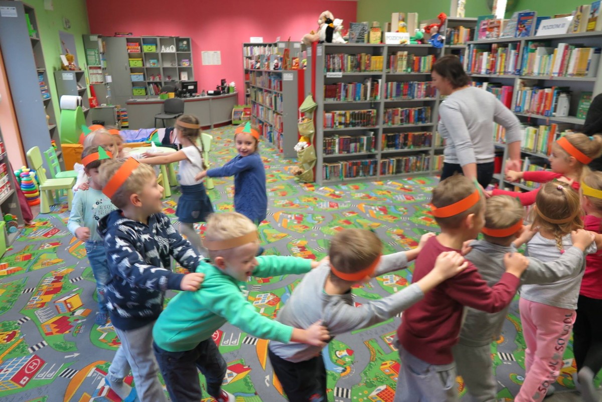 Wnętrze biblioteki. Grupa dzieci z Przedszkola "U Misia" uczestniczy w zabawie prowadzonej przez bibliotekarkę  Anię Wiśniewską.