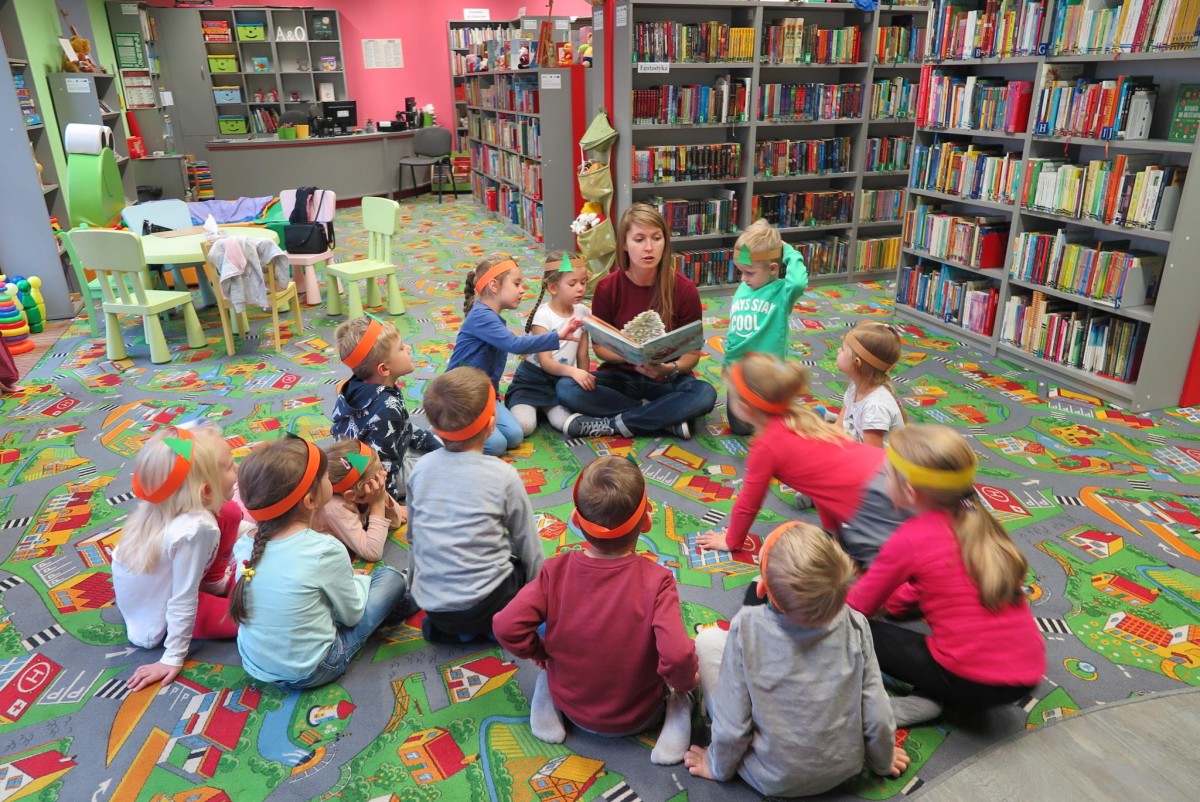 Wnętrze biblioteki. Grupa dzieci z Przedszkola "U Misia" słucha opowiadania "Prezent dla Świętego Mikołaja", czyta bibliotekarka Ola Cybulska.
