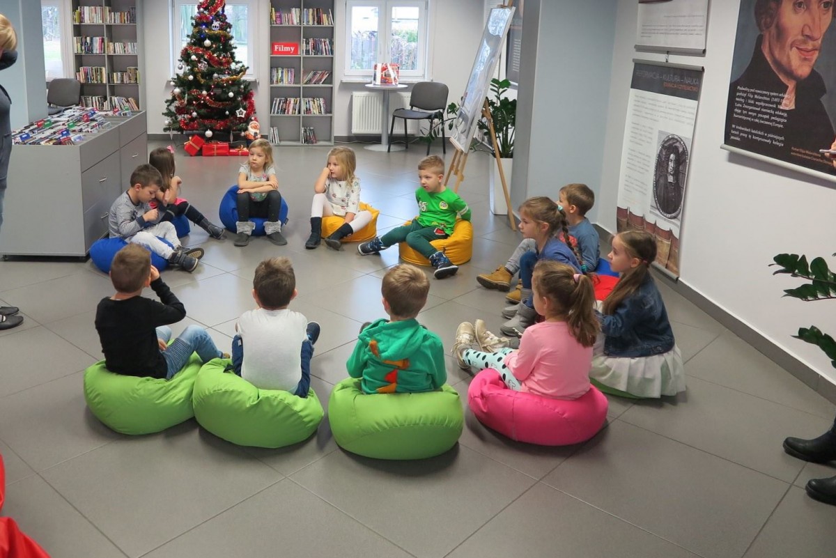 Wnętrze biblioteki,mediateka. Na pufach siedzą dzieci  „Kłapouszki” z Przedszkola „U Misia” uczą się programowania, mobilnych ozobotów.