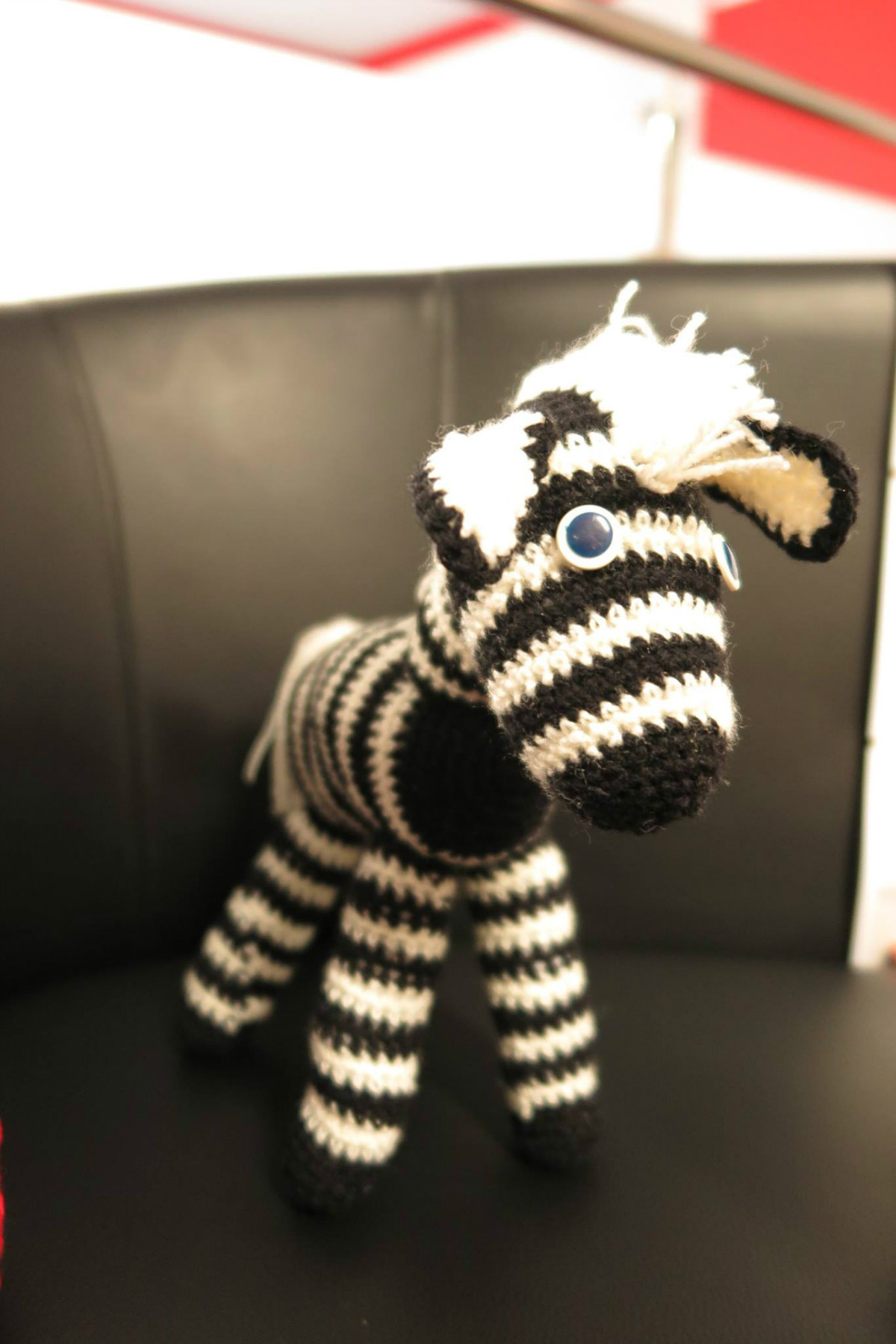 Na czarnej kanapie stoi zebra maskotka wykonana przez panie z Klubu Rękodzieła. 
