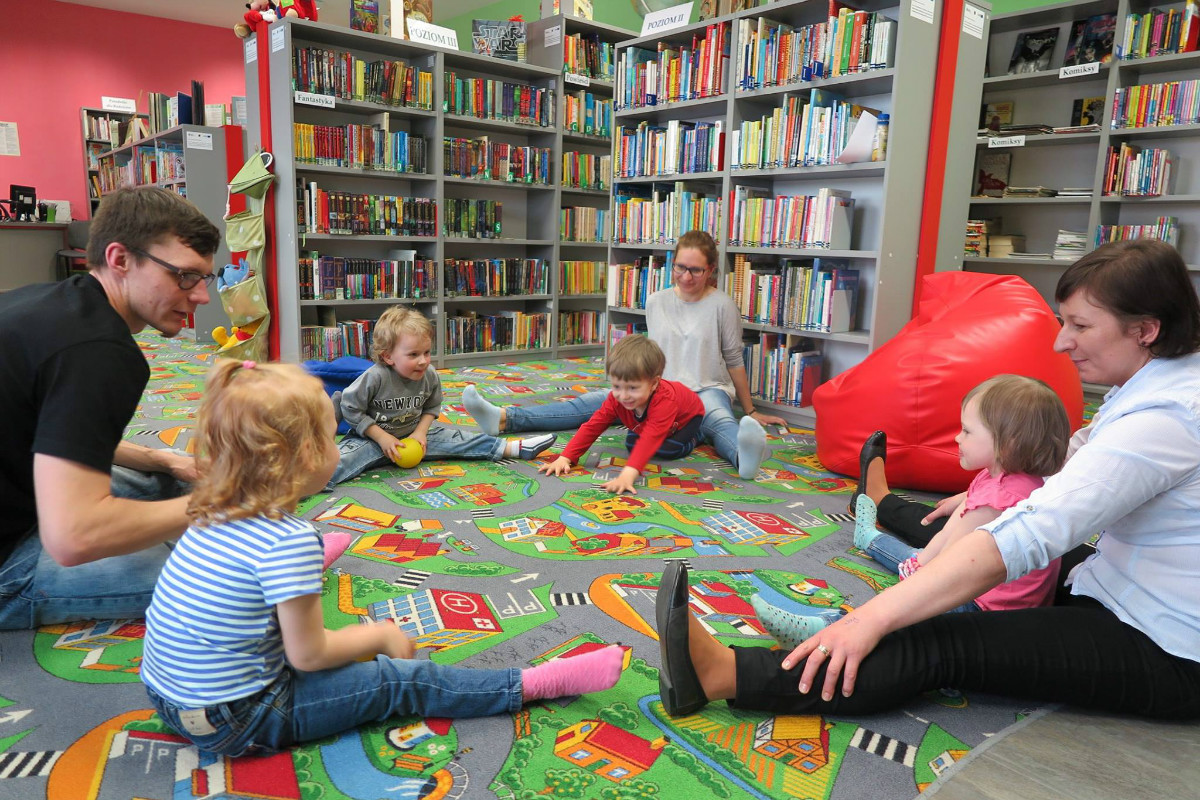 Grupa dzieci z bibliotekarka i opiekunami podczas zajęć w Klubie Malucha. 
