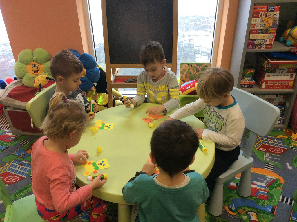 Przy stoliku siedzą dzieci wspólnie ozdabiają misie.
