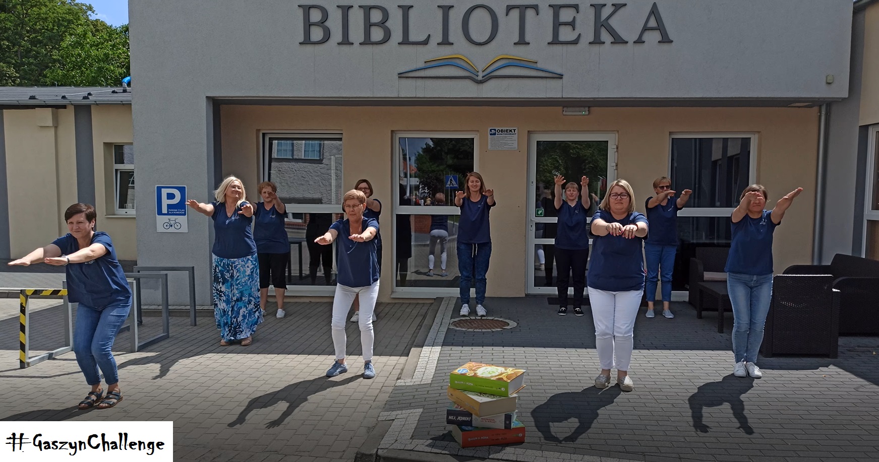 Przed biblioteką na placu 10 pracowników MBP w Działdowie została nominowana przez MGBP w Lidzbarku #Gaszyn Challenge do wykonania 10 przysiadów. 