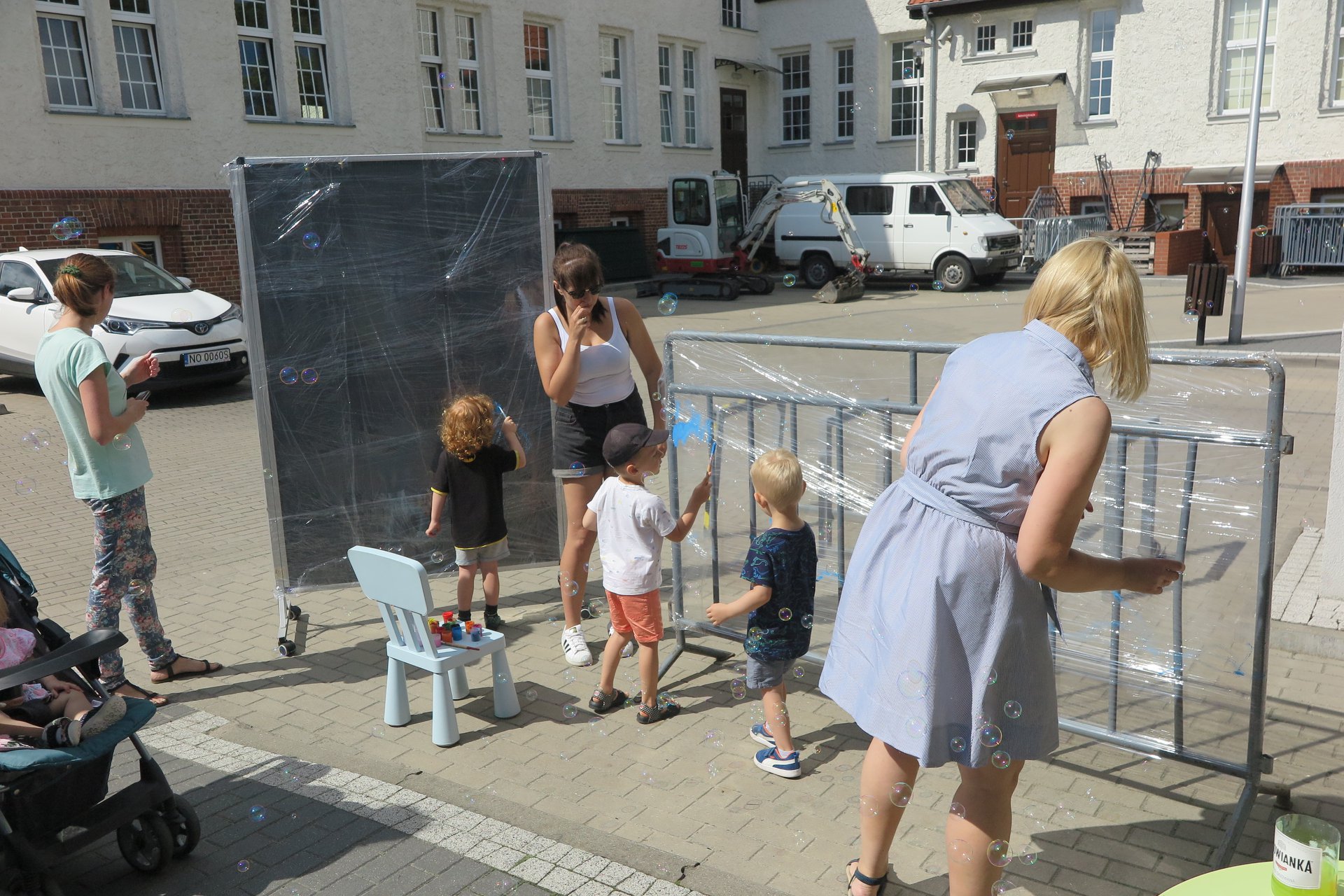 Przed budynkiem biblioteki w Działdowie troje dzieci oraz trzech opiekunów malują na folii motywy morskie. 