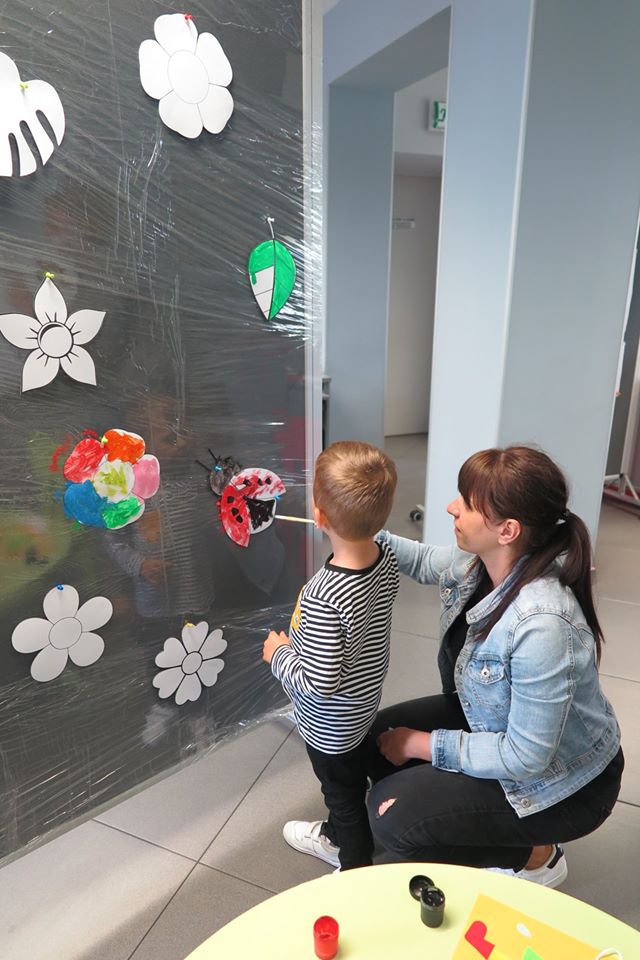 Wnętrze biblioteki opiekun wraz  z dzieckiem na banerze okrytym folią malują biedronkę. 