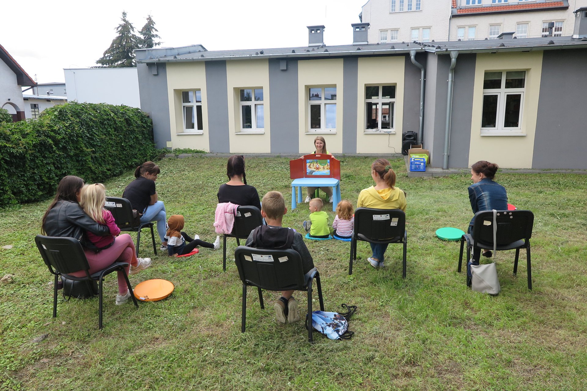 Na zielonym trawniku bibliotekarka Aleksandra Cybulska czyta bajkę pt.,, Przygody pingwina Pingo''. Pięcioro opiekunów siedzi na krzesełkach wraz z dziećmi. 