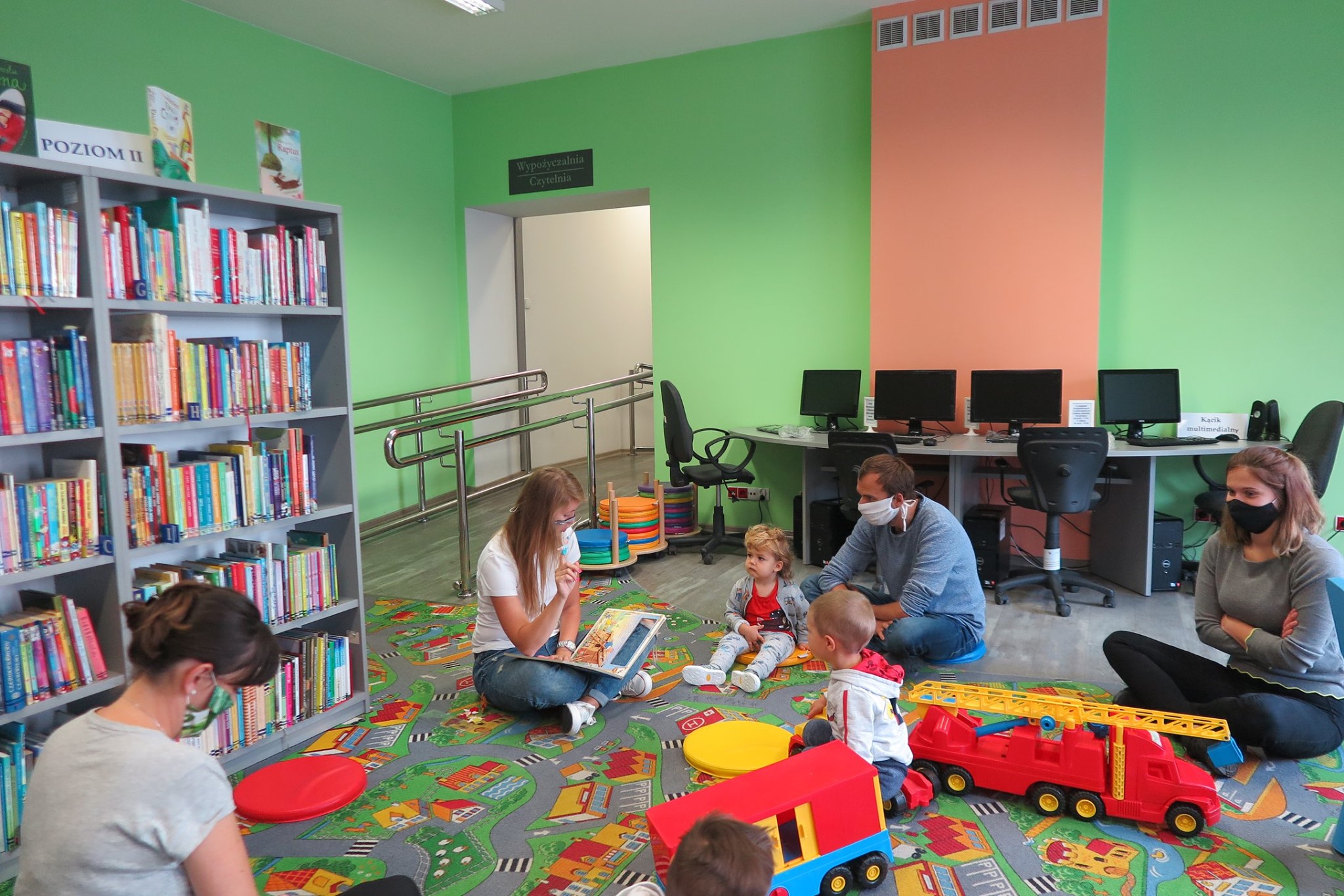 Wnętrze biblioteki (Klub Malucha) bibliotekarka Aleksandra Cybulska prowadzi zajęcia z dziećmi obok jest 3 opiekunów i zabawki.