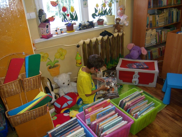 Wnętrze biblioteki, chłopiec bawi się zabawkami w tle regał z książkami.
